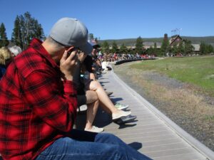 A crowd of people sitting along the deck that circle Old Faithful.