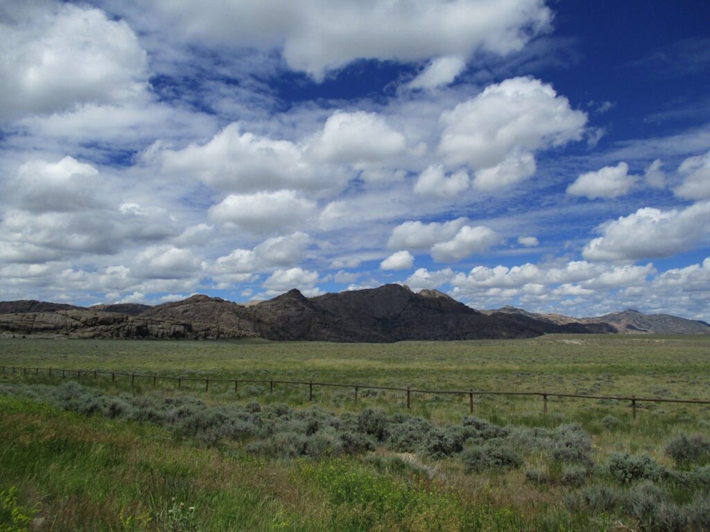 Fluffy clouds in a blue sky over a plain with granite mountains in the background.