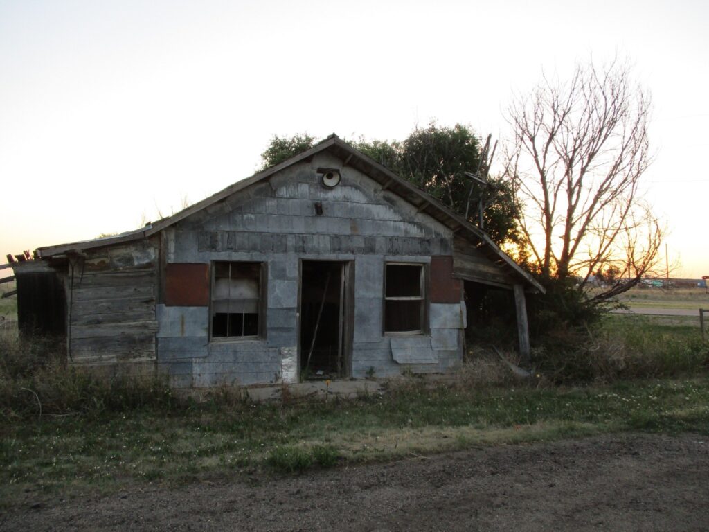 A small dilapidated one-story building with the sun setting in the background.
