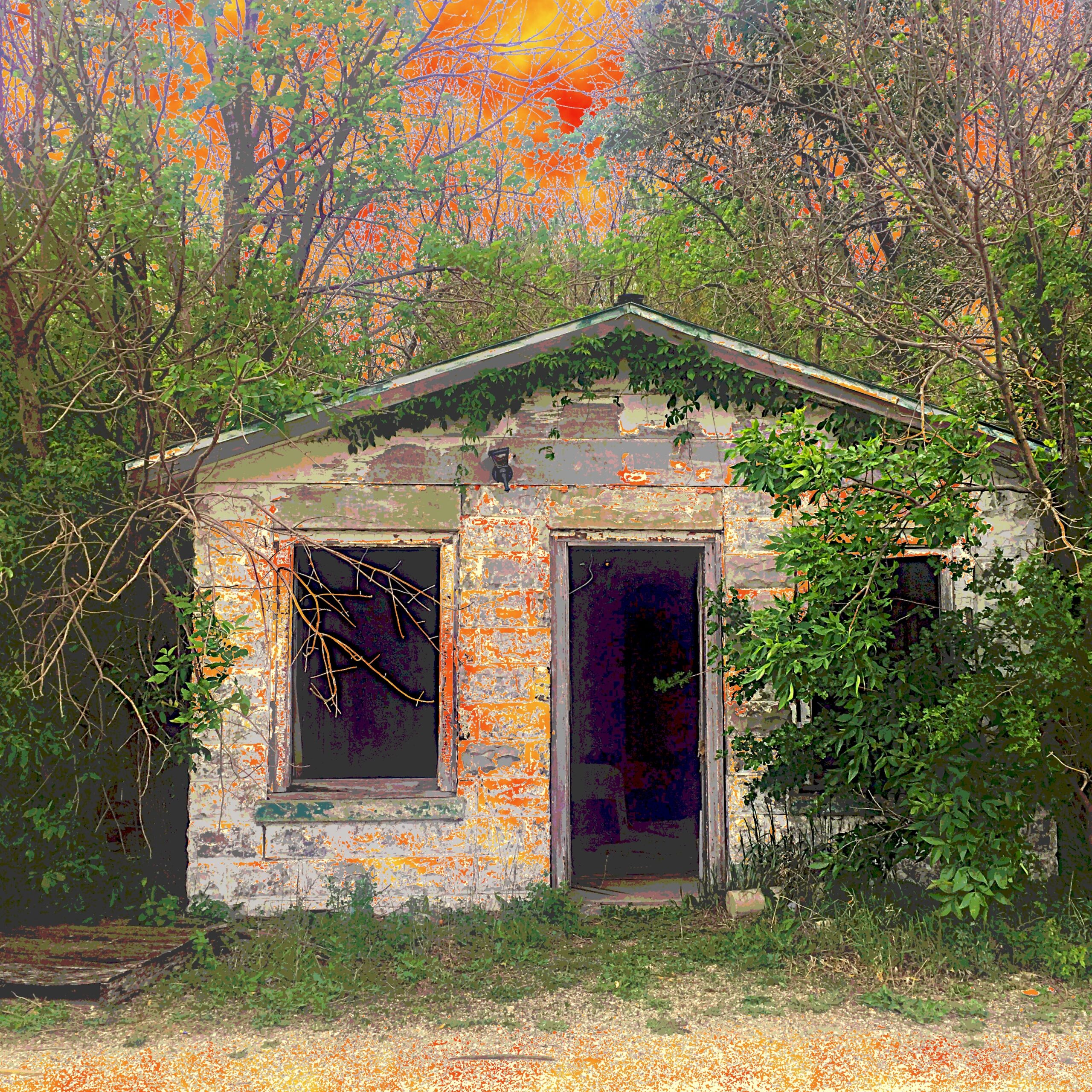 A small dilapidated building. The door is gone and so are the windows. It is very dark inside. Growing around it is the green of spring. The sky in the background is an angry red.